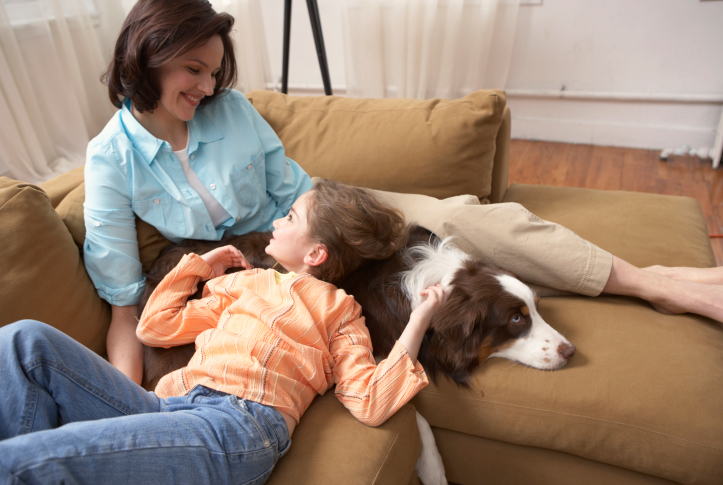 Mother with daughter (8-10) relaxing on sofa with dog
